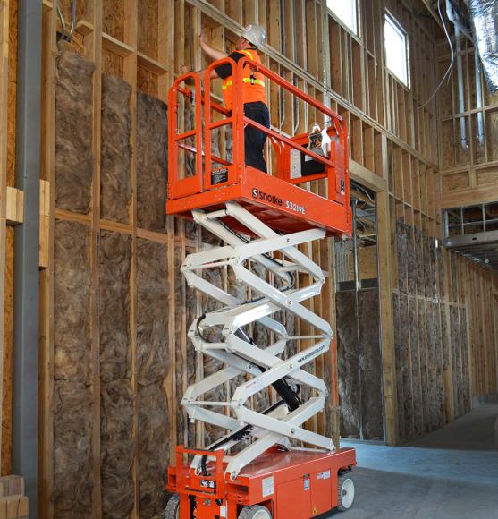 Operator in orange vest and hard hat standing in raised Snorkel S3219E inside a wood frame building