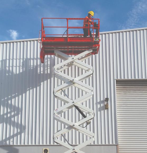 Operator in yellow hat using controls on elevated Snorkel orange and white scissor lift at industrial building