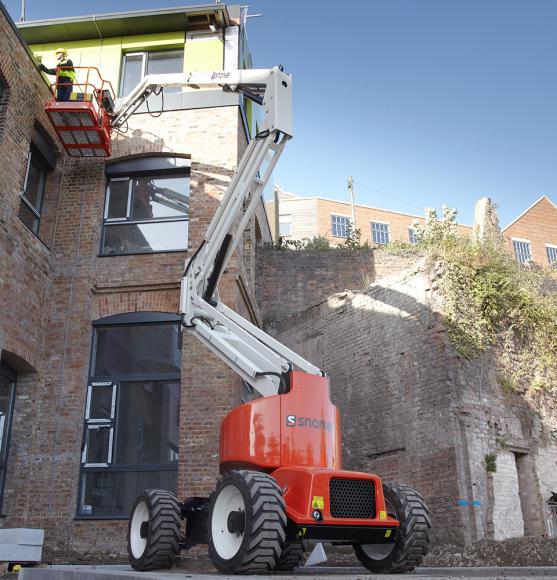 Orange and white boom lift on concrete with operator working at height on brick building
